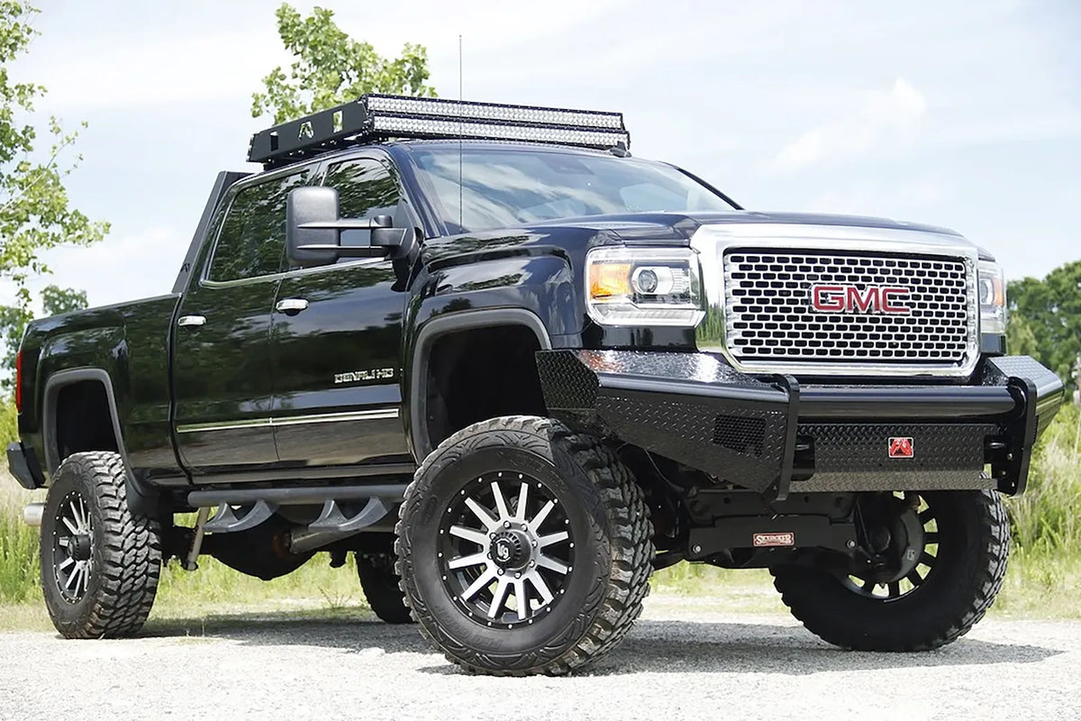 Fab Fours Black Steel front bumper on a black GMC Sierra 2500HD parked on gravel, front passenger-side three-quarter view, showing the no-guard diamond-plate face, top tube and wrapped wings
