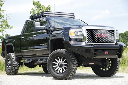 Fab Fours Black Steel front bumper on a black GMC Sierra 2500HD parked on gravel, front passenger-side three-quarter view, showing the no-guard diamond-plate face, top tube and wrapped wings