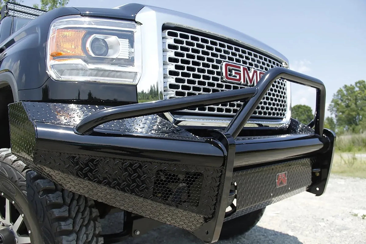 Fab Fours Black Steel front bumper with pre-runner guard on a black GMC Sierra 2500HD, outdoor close-up of the passenger-side corner, showing the pre-runner tube, diamond-plate wing and honeycomb light opening
