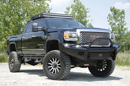 Fab Fours Black Steel front bumper with pre-runner guard on a black GMC Sierra 2500HD parked on gravel, front passenger-side three-quarter view, showing the pre-runner hoop, diamond-plate face and wrapped wings
