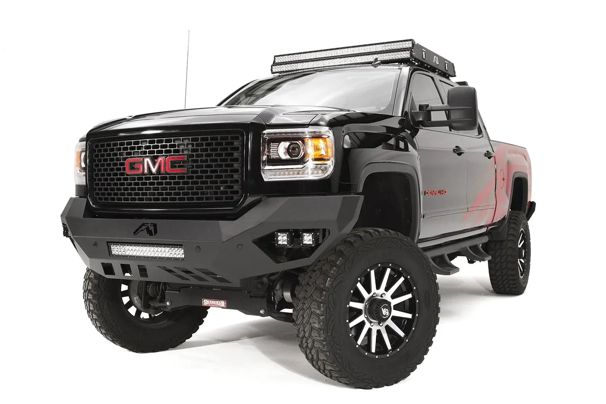 Fab Fours Vengeance front bumper on a black GMC Sierra 2500HD, front driver-side three-quarter view, showing the sculpted no-guard face, LED light bar and angular skid section