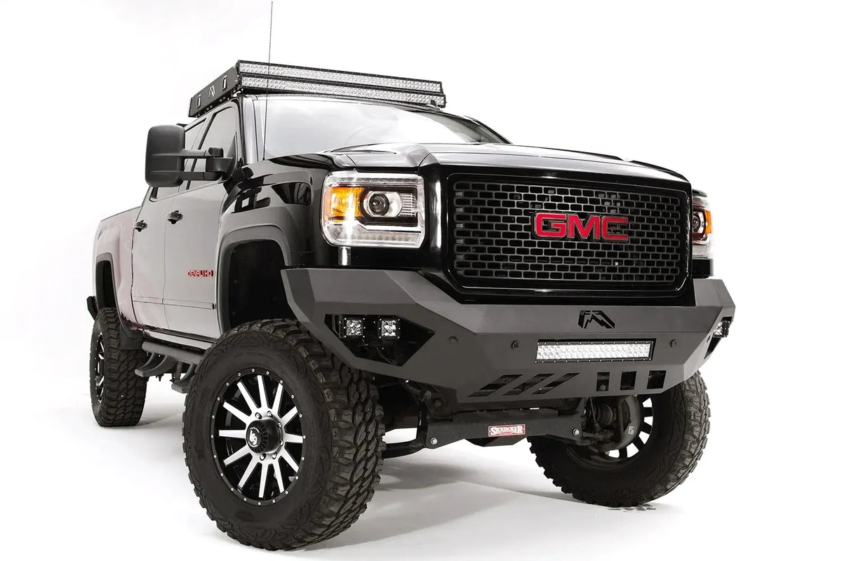 Fab Fours Vengeance front bumper on a black GMC Sierra 2500HD, front passenger-side three-quarter view, showing the sculpted no-guard face, integrated LED light bar and cube light pockets