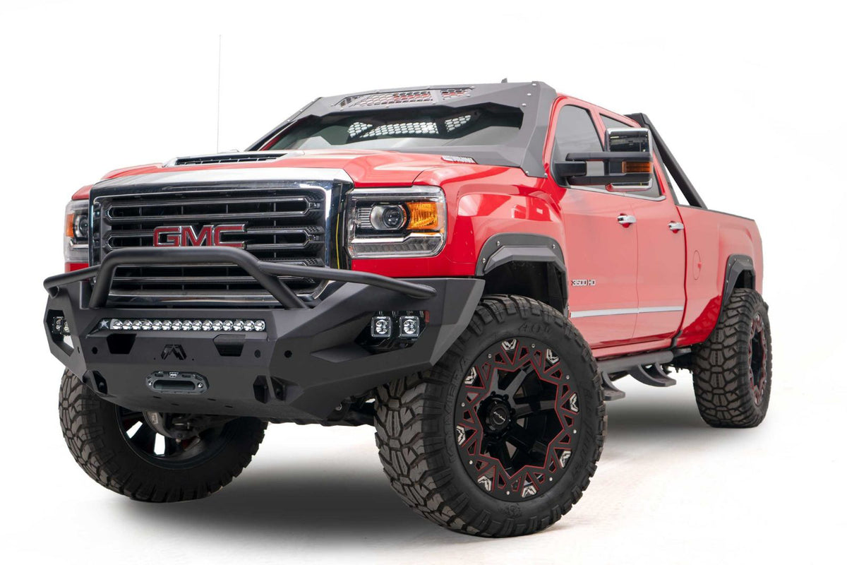 Fab Fours Matrix front bumper with pre-runner guard on a red GMC Sierra 2500HD/3500HD, front driver-side three-quarter view, showing pre-runner hoop, integrated light bar, cube light pods, winch-ready center