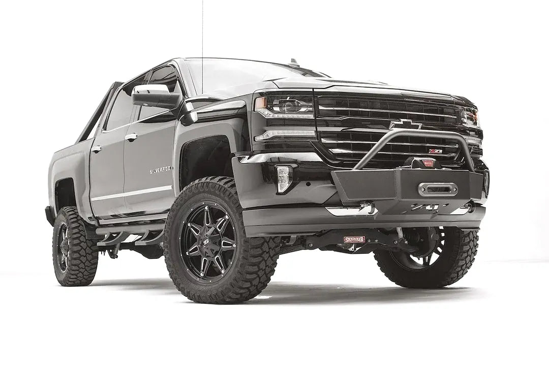 Fab Fours winch mount on a black and gray Chevrolet Silverado 1500, front passenger-side three-quarter view, showing tubular hoop, winch plate, low-profile mounting under the factory bumper