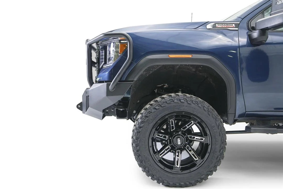 Fab Fours Premium Winch front bumper with full guard on a blue and gray GMC Sierra 2500HD/3500HD, close-up of the front corner, showing guard upright, bumper end cap, wheel-well clearance