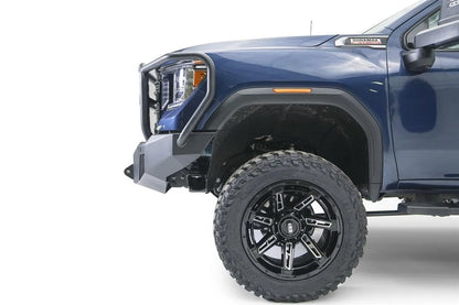 Fab Fours Premium Winch front bumper with full guard on a blue and gray GMC Sierra 2500HD/3500HD, close-up of the front corner, showing guard upright, bumper end cap, wheel-well clearance