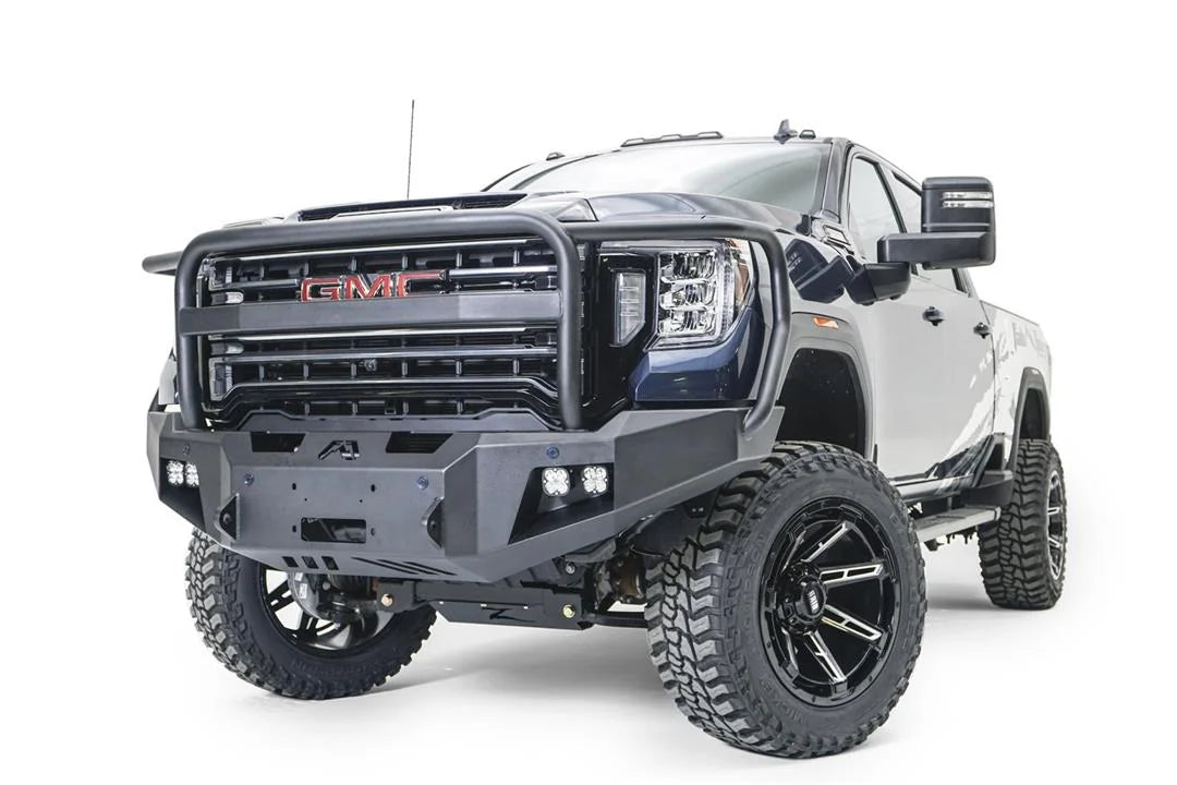 Fab Fours Premium Winch front bumper with full guard on a blue and gray GMC Sierra 2500HD/3500HD, front driver-side three-quarter view, showing full guard hoop, winch mount opening, cube light pods, angled end caps