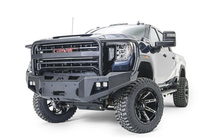 Fab Fours Premium Winch front bumper with full guard on a blue and gray GMC Sierra 2500HD/3500HD, front driver-side three-quarter view, showing full guard hoop, winch mount opening, cube light pods, angled end caps