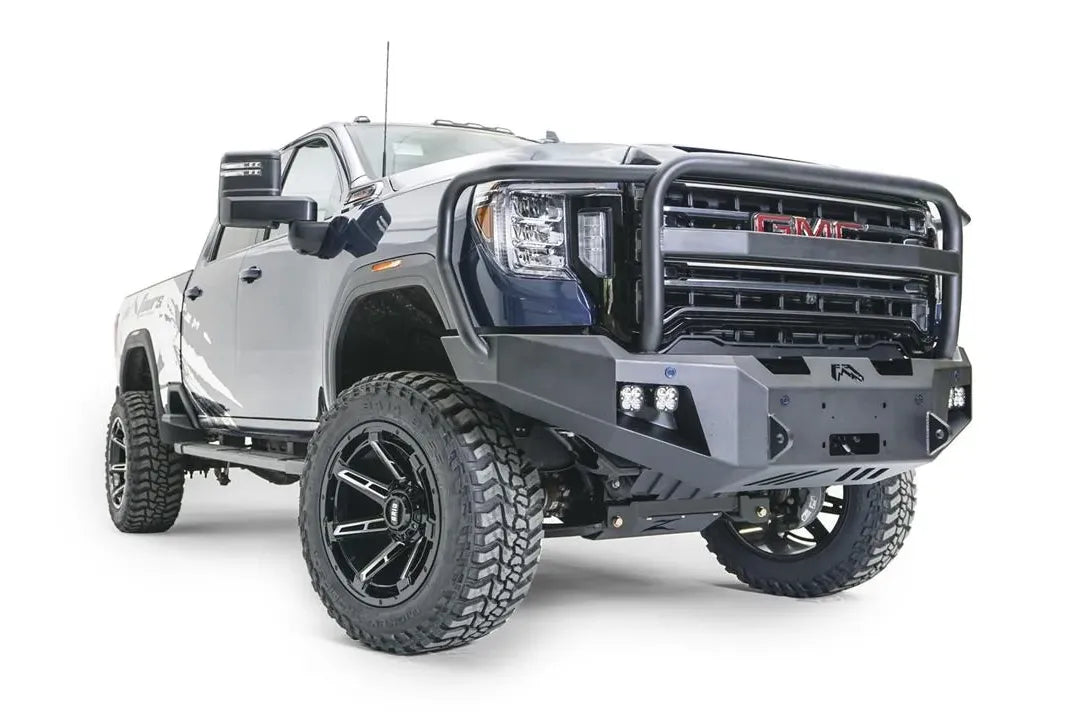 Fab Fours Premium Winch front bumper with full guard on a blue and gray GMC Sierra 2500HD/3500HD, front passenger-side three-quarter view, showing full guard hoop, winch mount opening, cube light pods, angled end caps