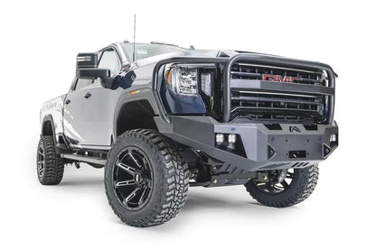 Fab Fours Premium Winch front bumper with full guard on a blue and gray GMC Sierra 2500HD/3500HD, front passenger-side three-quarter view, showing full guard hoop, winch mount opening, cube light pods, angled end caps