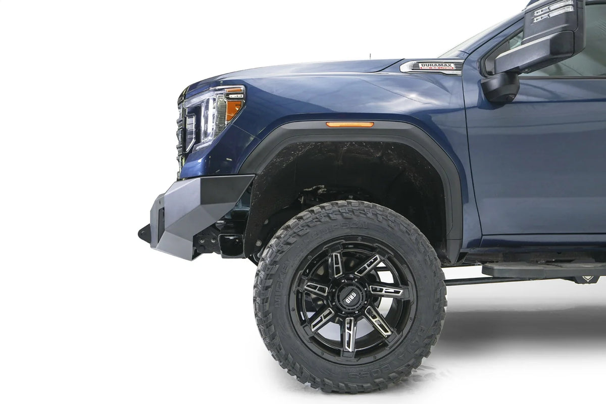 Fab Fours Premium Winch front bumper on a blue and gray GMC Sierra 2500HD/3500HD, close-up of the front corner, showing bumper end cap profile, wheel-well clearance