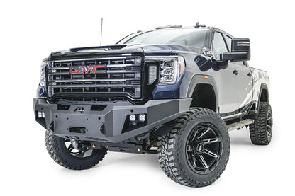Fab Fours Premium Winch front bumper on a blue and gray GMC Sierra 2500HD/3500HD, front driver-side three-quarter view, showing winch mount opening, cube light pods, angled end caps