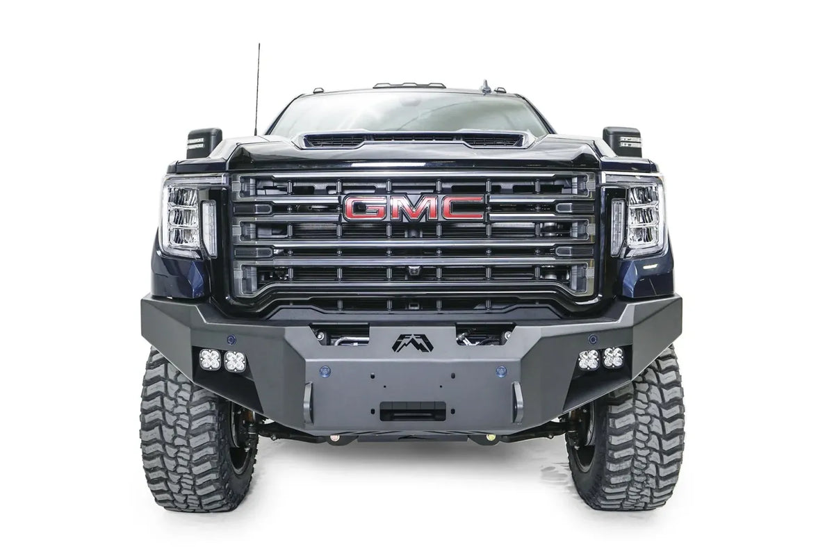 Fab Fours Premium Winch front bumper on a blue and gray GMC Sierra 2500HD/3500HD, straight-on front view, showing winch mount opening, cube light pods, angled end caps
