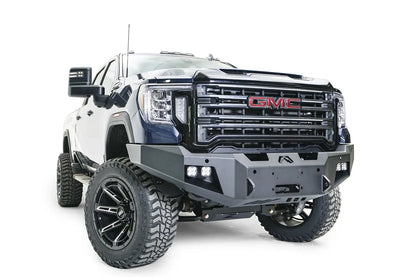 Fab Fours Premium Winch front bumper on a blue and gray GMC Sierra 2500HD/3500HD, front passenger-side three-quarter view, showing winch mount opening, cube light pods, angled end caps