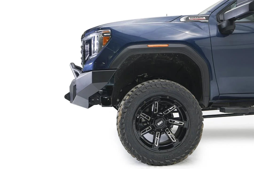 Fab Fours Premium Winch front bumper with pre-runner guard on a blue and gray GMC Sierra 2500HD/3500HD, close-up of the front corner, showing pre-runner hoop, bumper end cap profile, wheel-well clearance