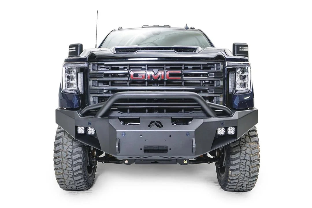 Fab Fours Premium Winch front bumper with pre-runner guard on a blue and gray GMC Sierra 2500HD/3500HD, straight-on front view, showing pre-runner hoop, winch mount opening, cube light pods