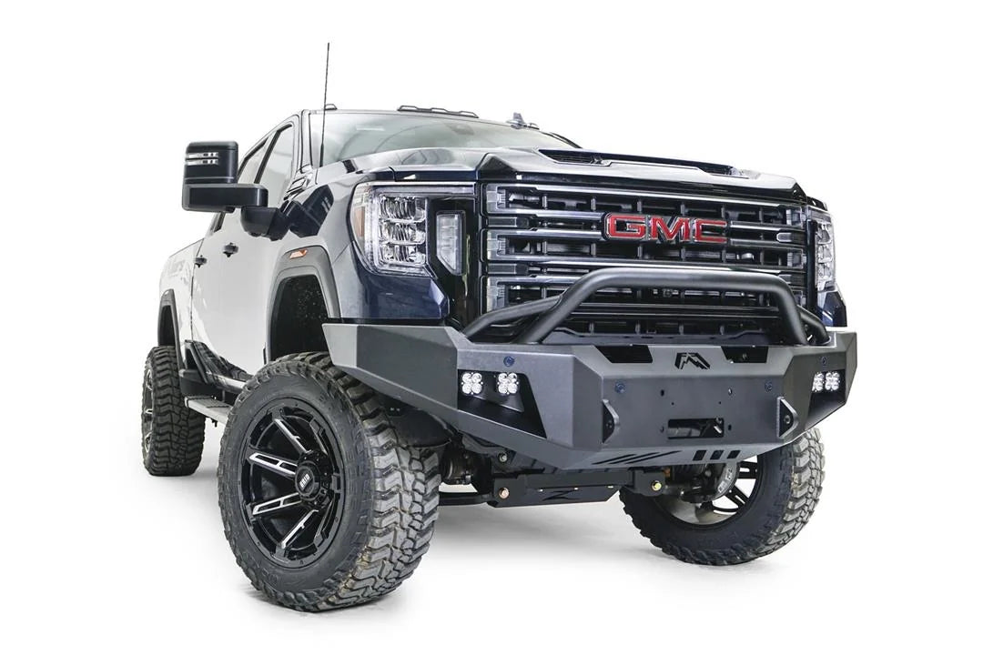Fab Fours Premium Winch front bumper with pre-runner guard on a blue and gray GMC Sierra 2500HD/3500HD, front passenger-side three-quarter view, showing pre-runner hoop, winch mount opening, cube light pods