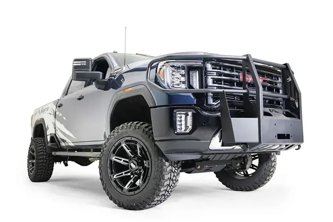 Fab Fours winch mount with full guard on a blue and gray GMC Sierra 2500HD/3500HD, front passenger-side three-quarter view, showing full guard uprights, wraparound headlight hoops, winch plate