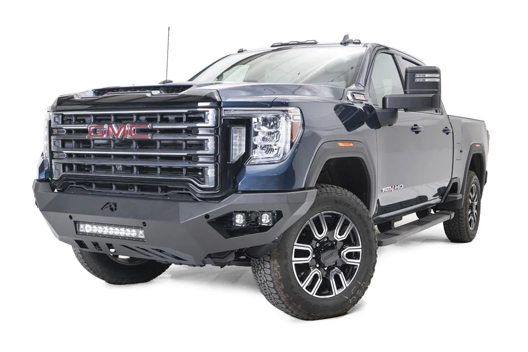 Fab Fours Vengeance front bumper on a blue GMC Sierra 2500HD/3500HD, front driver-side three-quarter view, showing integrated light bar, cube light pods, angular skid plate