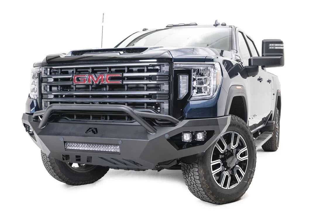 Fab Fours Vengeance front bumper with pre-runner guard on a blue GMC Sierra 2500HD/3500HD, front driver-side three-quarter view, showing pre-runner hoop, integrated light bar, cube light pods, angular skid plate