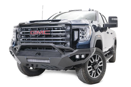 Fab Fours Vengeance front bumper with pre-runner guard on a blue GMC Sierra 2500HD/3500HD, front driver-side three-quarter view, showing pre-runner hoop, integrated light bar, cube light pods, angular skid plate