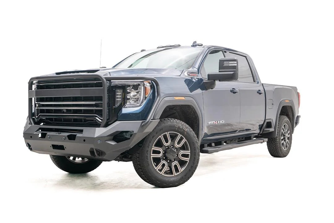 Fab Fours Matrix front bumper with full guard on a blue GMC Sierra 2500HD/3500HD, front driver-side three-quarter view, showing full grille guard, winch-ready center, cube light pods