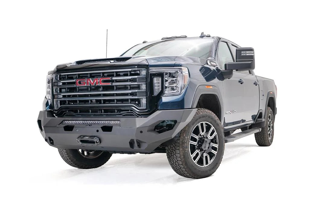 Fab Fours Matrix front bumper on a blue GMC Sierra 2500HD/3500HD, front driver-side three-quarter view, showing integrated light bar, winch-ready center, cube light pods