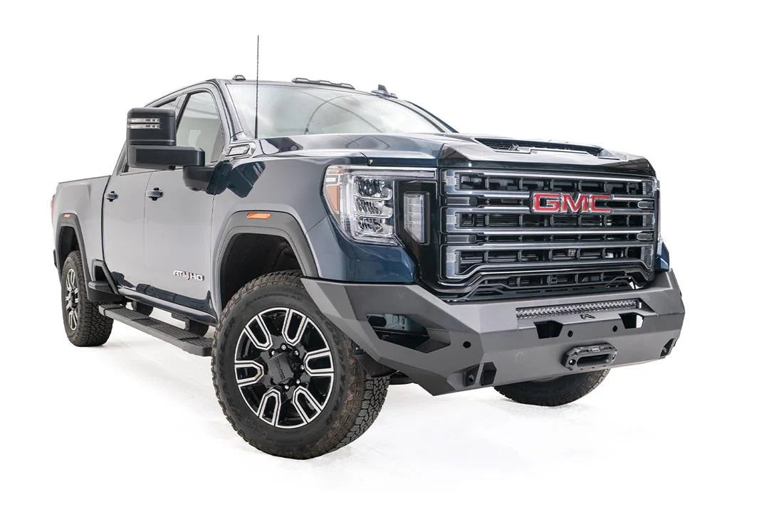 Fab Fours Matrix front bumper on a blue GMC Sierra 2500HD/3500HD, front passenger-side three-quarter view, showing integrated light bar, winch-ready center, cube light pods