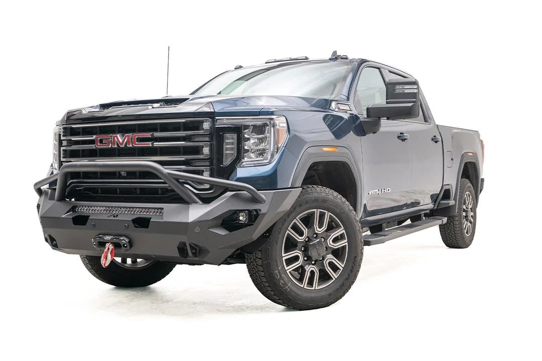 Fab Fours Matrix front bumper with pre-runner guard on a blue GMC Sierra 2500HD/3500HD, front driver-side three-quarter view, showing pre-runner hoop, integrated light bar, winch-ready center
