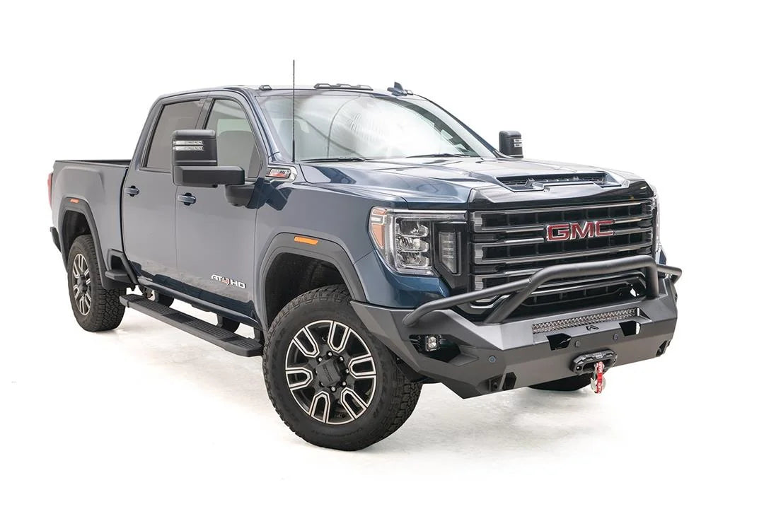 Fab Fours Matrix front bumper with pre-runner guard on a blue GMC Sierra 2500HD/3500HD, front passenger-side three-quarter view, showing pre-runner hoop, integrated light bar, winch-ready center