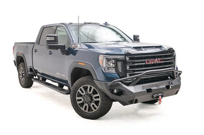 Fab Fours Matrix front bumper with pre-runner guard on a blue GMC Sierra 2500HD/3500HD, front passenger-side three-quarter view, showing pre-runner hoop, integrated light bar, winch-ready center