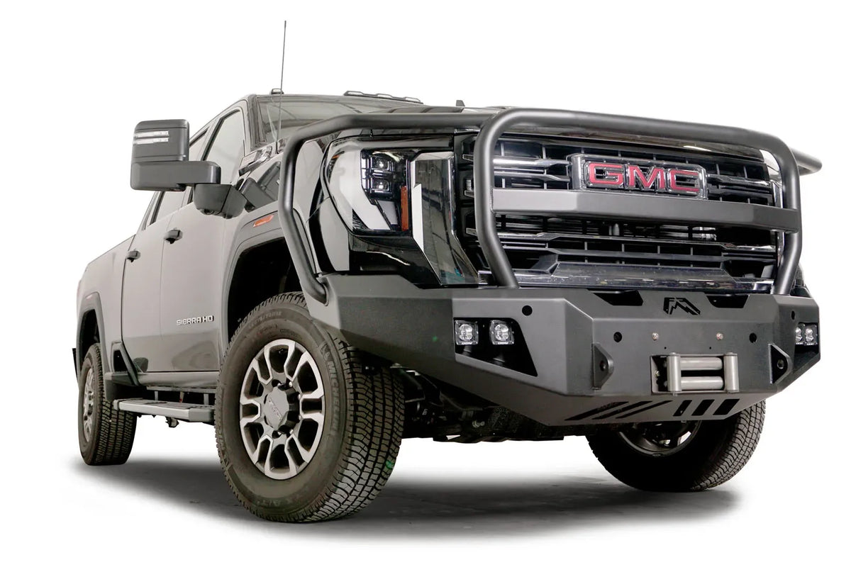 Fab Fours Premium Winch front bumper with full guard on a black GMC Sierra 2500HD/3500HD, front passenger-side three-quarter view, showing full guard hoop, winch mount, cube light pods, angled end caps