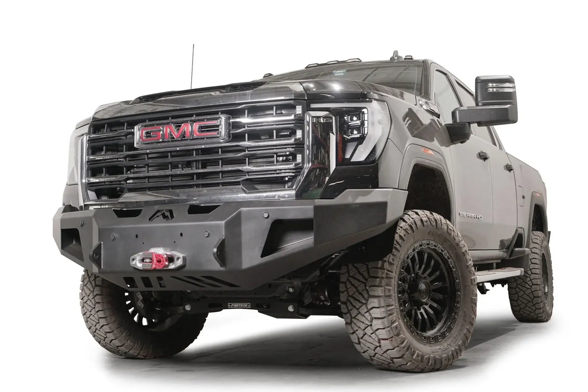 Fab Fours Premium Winch front bumper on a black GMC Sierra 2500HD/3500HD, front driver-side three-quarter view, showing winch mount, cube light pods, angled end caps