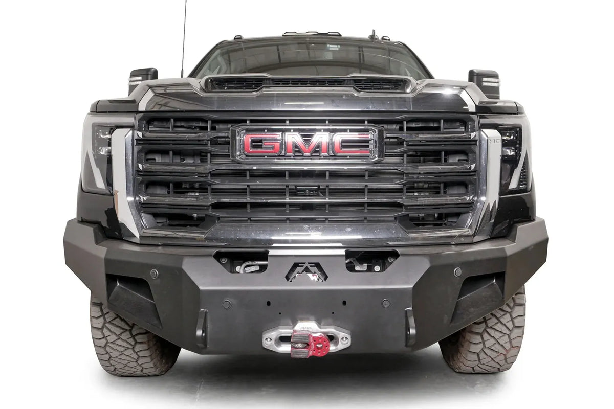 Fab Fours Premium Winch front bumper on a black GMC Sierra 2500HD/3500HD, straight-on front view, showing winch mount, cube light pods, angled end caps