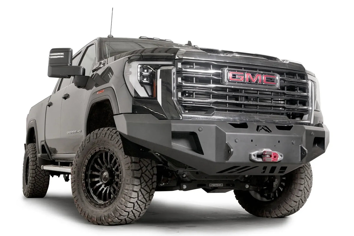 Fab Fours Premium Winch front bumper on a black GMC Sierra 2500HD/3500HD, front passenger-side three-quarter view, showing winch mount, cube light pods, angled end caps