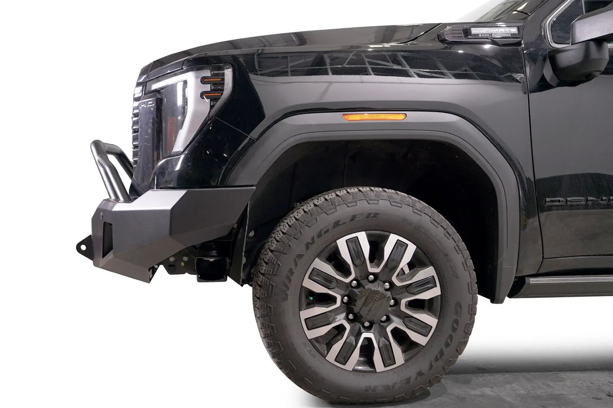 Fab Fours Premium Winch front bumper with pre-runner guard on a black GMC Sierra 2500HD/3500HD, close-up of the front corner, showing pre-runner hoop, bumper end cap profile, wheel-well clearance