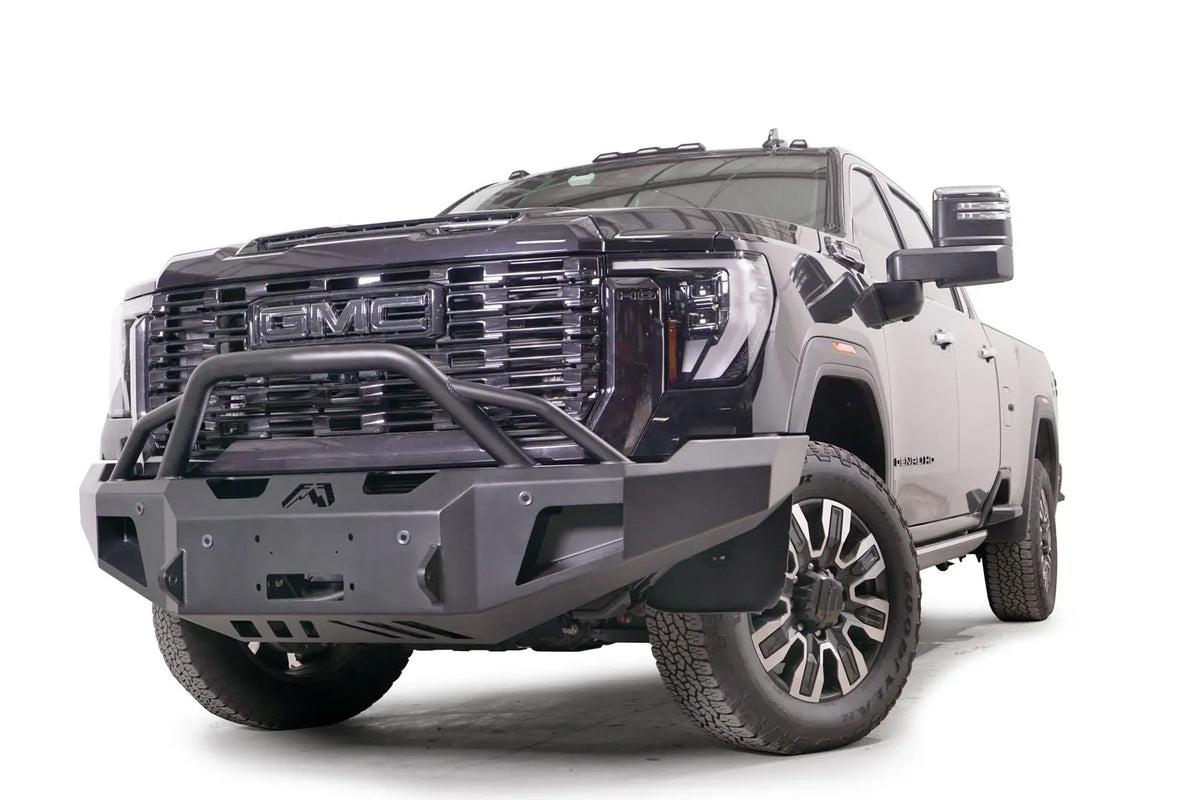 Fab Fours Premium Winch front bumper with pre-runner guard on a black GMC Sierra 2500HD/3500HD, front driver-side three-quarter view, showing pre-runner hoop, winch mount opening, angled end caps