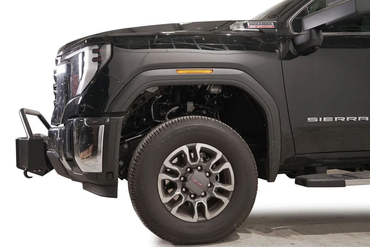 Fab Fours winch mount with pre-runner guard on a black GMC Sierra 2500HD/3500HD, close-up of the front corner, showing pre-runner hoop, winch mount profile, wheel-well clearance