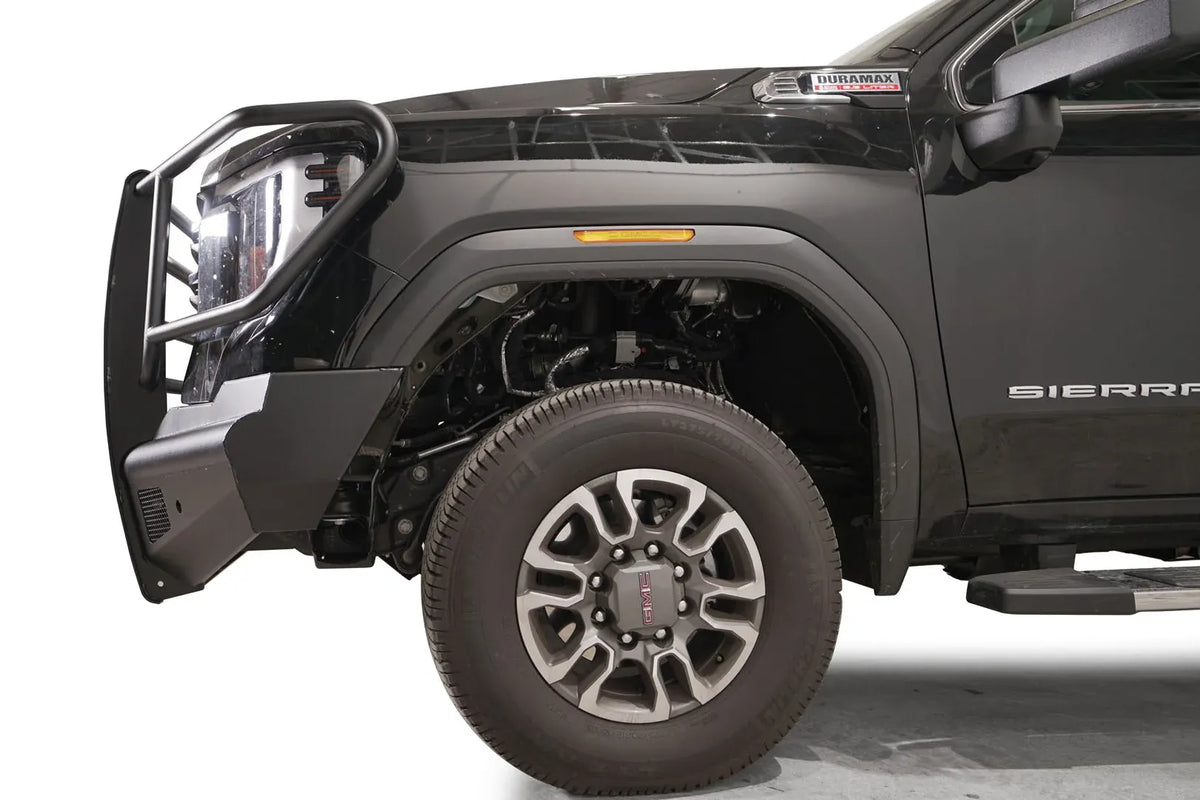 Fab Fours Black Steel Elite front bumper with full guard on a black GMC Sierra 2500HD/3500HD, close-up of the front corner, showing full guard side hoop, bumper end profile, wheel-well clearance