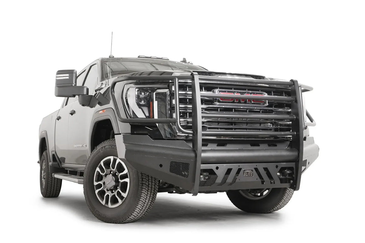 Fab Fours Black Steel Elite front bumper with full guard on a black GMC Sierra 2500HD/3500HD, front passenger-side three-quarter view, showing full grille guard, Elite badge, slotted skid plate, mesh end inserts