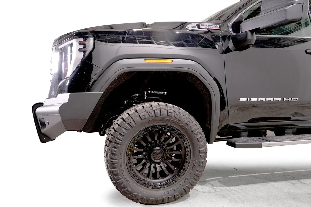 Fab Fours Black Steel Elite front bumper on a black GMC Sierra 2500HD/3500HD, close-up of the front corner, showing bumper end profile, wheel-well clearance