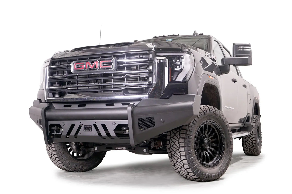 Fab Fours Black Steel Elite front bumper on a black GMC Sierra 2500HD/3500HD, front driver-side three-quarter view, showing Elite badge, slotted skid plate, mesh end inserts, top tube