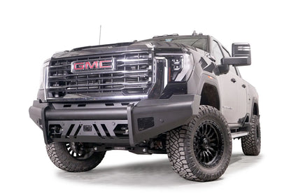 Fab Fours Black Steel Elite front bumper on a black GMC Sierra 2500HD/3500HD, front driver-side three-quarter view, showing Elite badge, slotted skid plate, mesh end inserts, top tube
