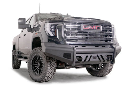 Fab Fours Black Steel Elite front bumper on a black GMC Sierra 2500HD/3500HD, front passenger-side three-quarter view, showing Elite badge, slotted skid plate, mesh end inserts, top tube