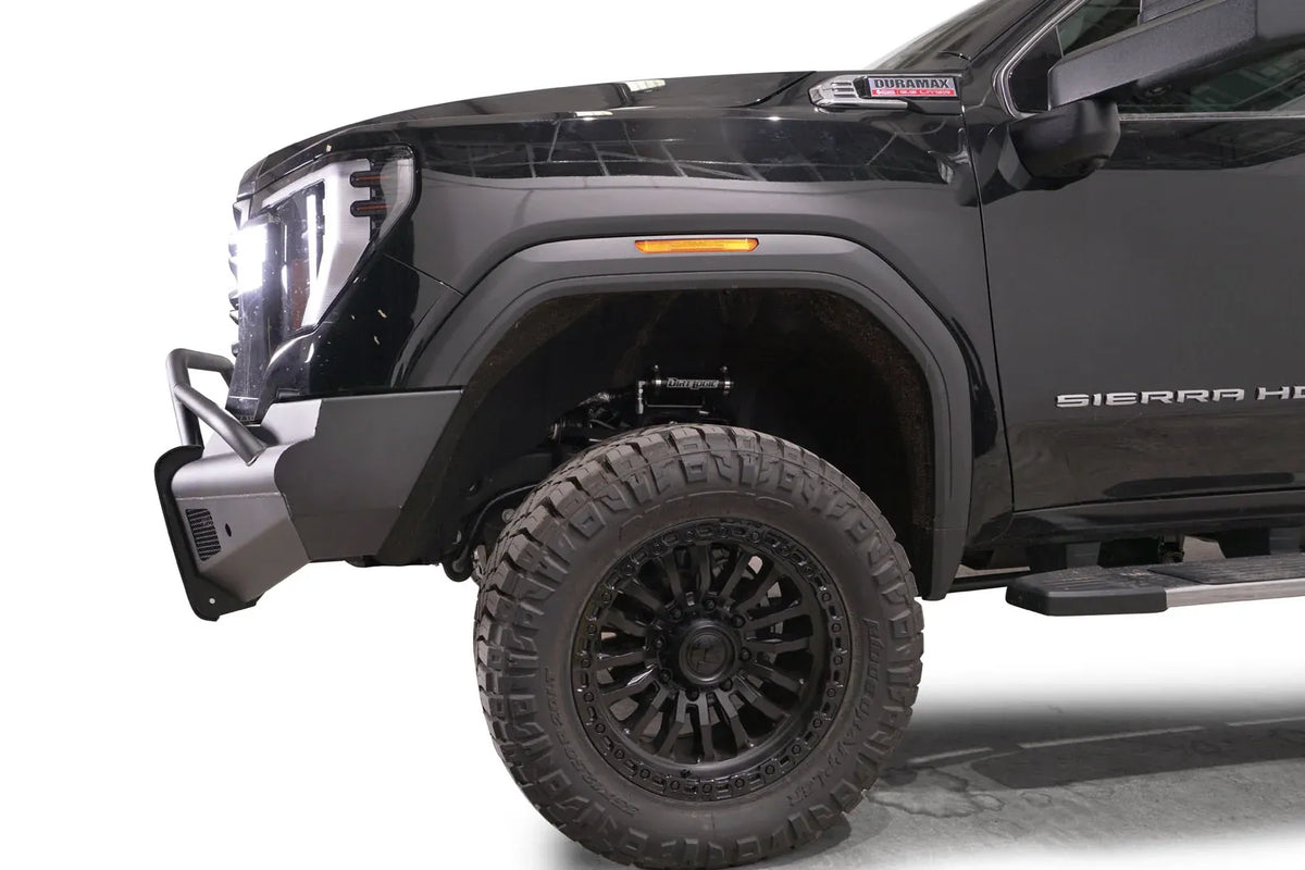 Fab Fours Black Steel Elite front bumper with pre-runner guard on a black GMC Sierra 2500HD/3500HD, close-up of the front corner, showing pre-runner hoop, bumper end profile, wheel-well clearance