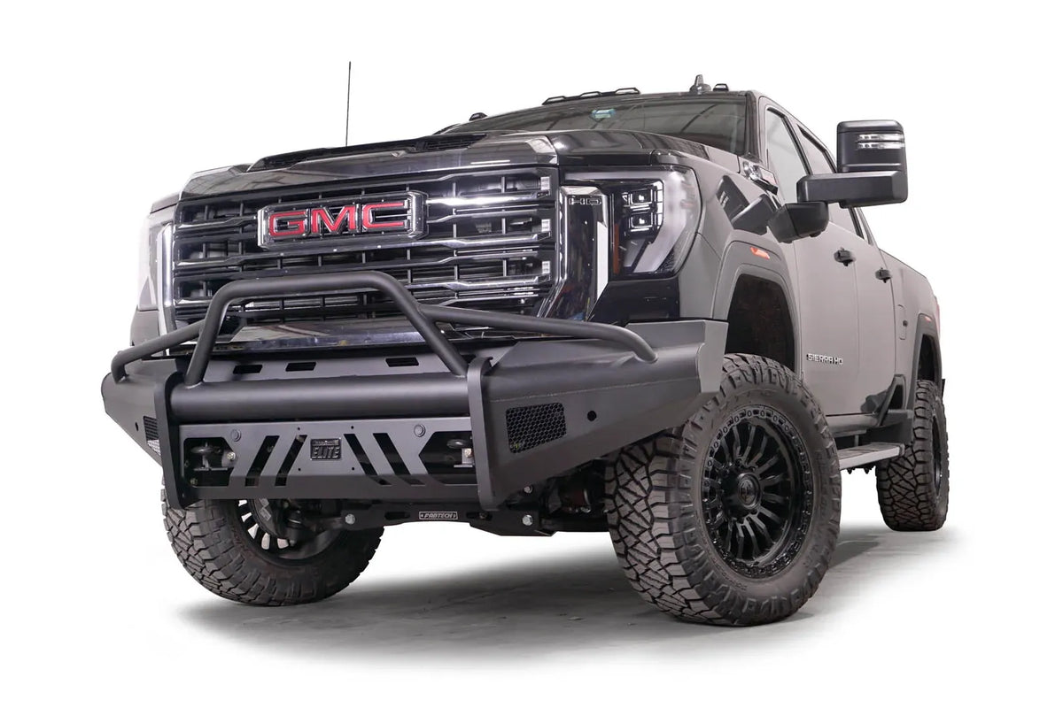Fab Fours Black Steel Elite front bumper with pre-runner guard on a black GMC Sierra 2500HD/3500HD, front driver-side three-quarter view, showing pre-runner hoop, Elite badge, slotted skid plate, mesh end inserts