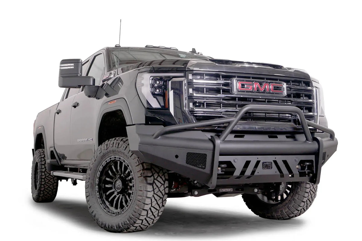 Fab Fours Black Steel Elite front bumper with pre-runner guard on a black GMC Sierra 2500HD/3500HD, front passenger-side three-quarter view, showing pre-runner hoop, Elite badge, slotted skid plate, mesh end inserts
