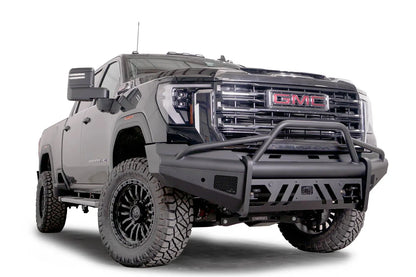 Fab Fours Black Steel Elite front bumper with pre-runner guard on a black GMC Sierra 2500HD/3500HD, front passenger-side three-quarter view, showing pre-runner hoop, Elite badge, slotted skid plate, mesh end inserts