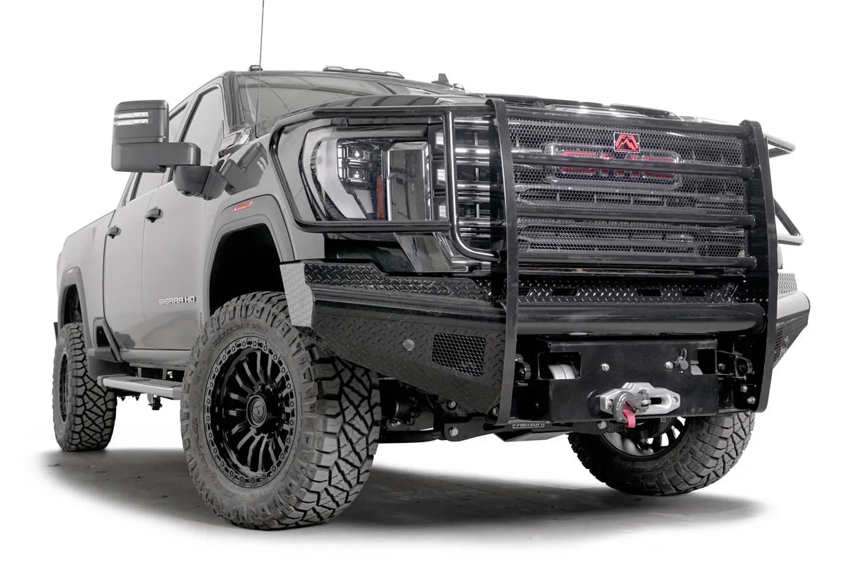 Fab Fours Black Steel front bumper with full guard on a black GMC Sierra 2500HD/3500HD, front passenger-side three-quarter view, showing full grille guard, diamond-plate finish, mesh end inserts, winch