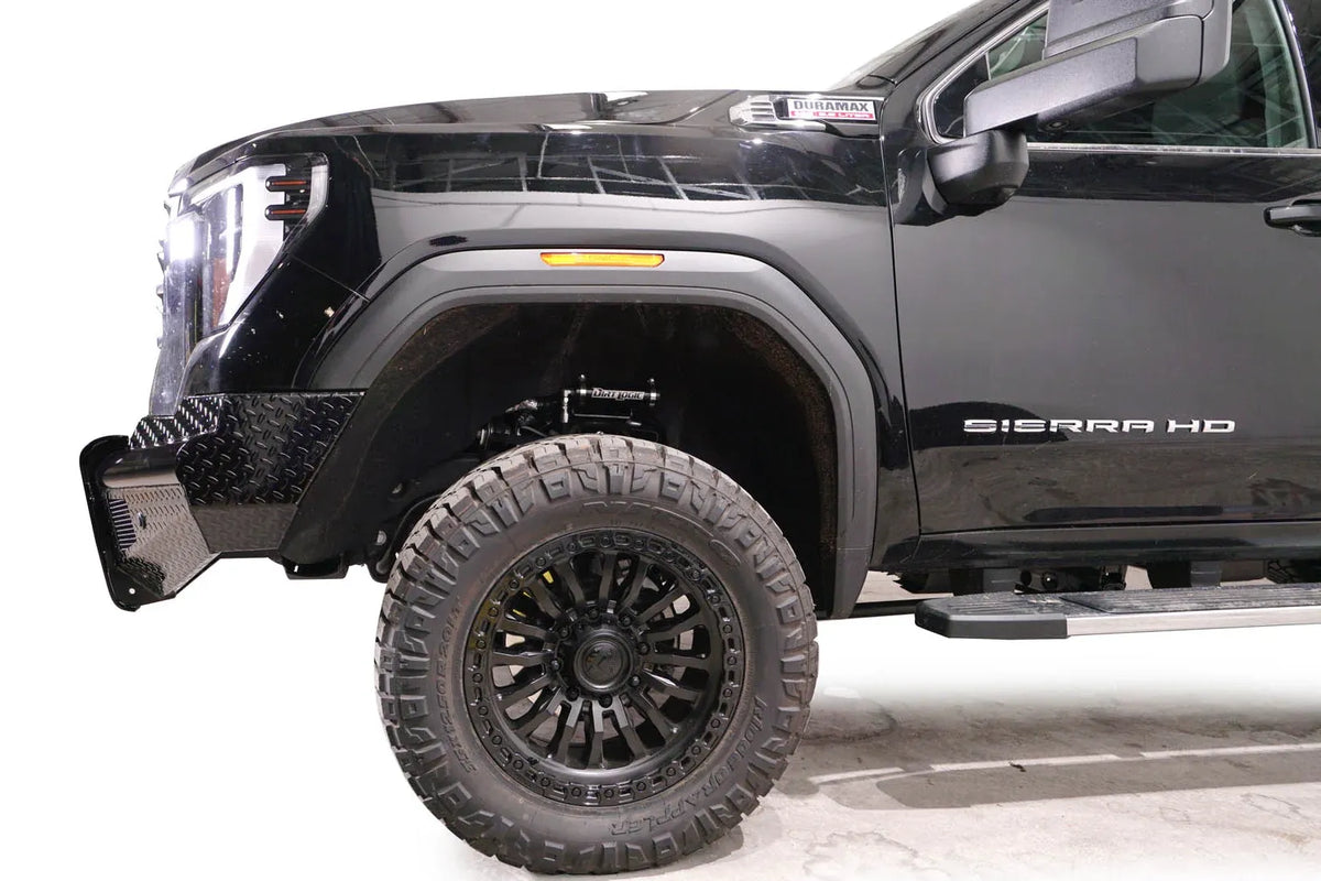 Fab Fours Black Steel front bumper on a black GMC Sierra 2500HD/3500HD, close-up of the front corner, showing diamond-plate end, top tube, wheel-well clearance